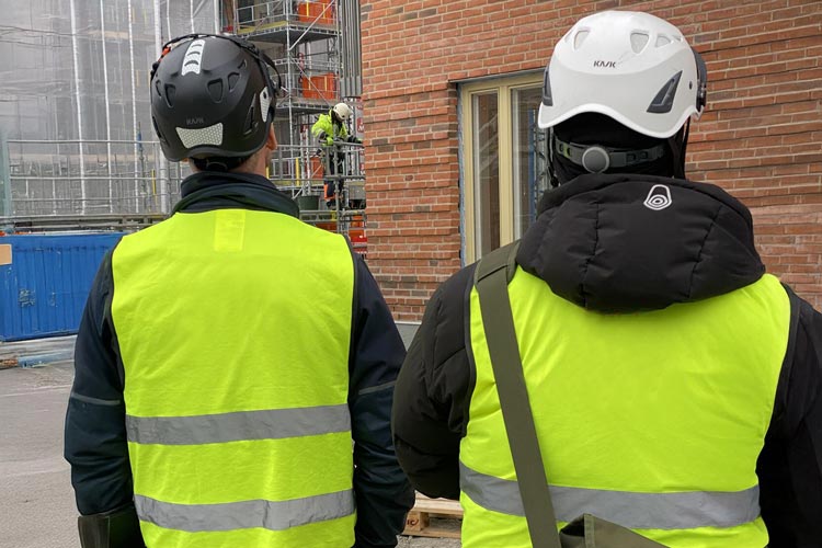 Två män i gula västar tittar ut mot byggnad